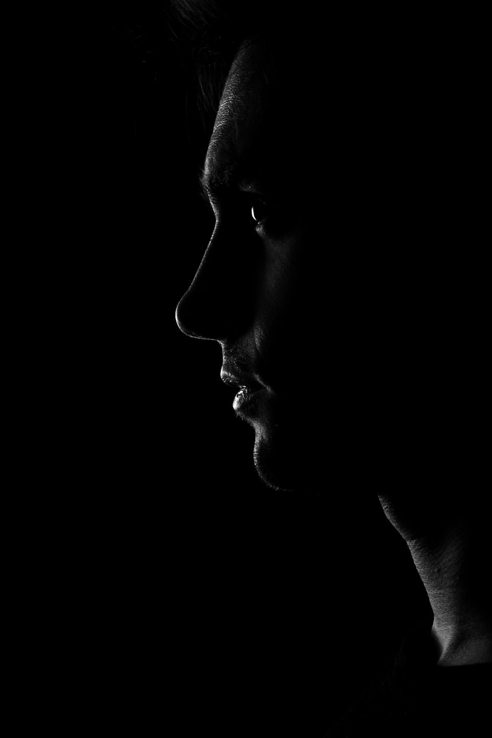Profilo del viso di una persona illuminato da luce laterale su sfondo scuro.
